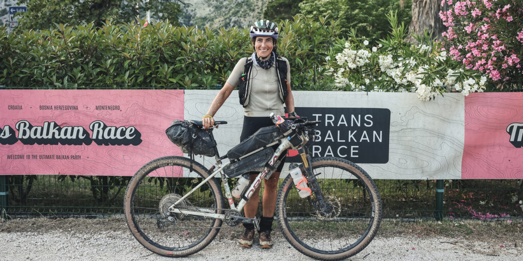 Gloworm athlete Dilara Tuna with her bike at the 2025 Trans Balkan Race, smiling after completing the 1400km off-road route through the Balkans.