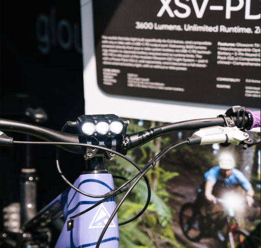 Gloworm XSV-PD Light System mounted on handlebars at the Gloworm Lights booth, Sea Otter Classic 2026, with 3600 Lumens display panel in the background.